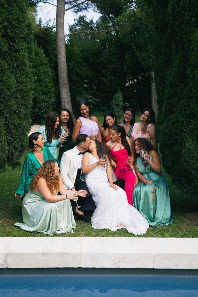 wedding group portrait turning into natural moment with couple kissing surrounded by guests provence